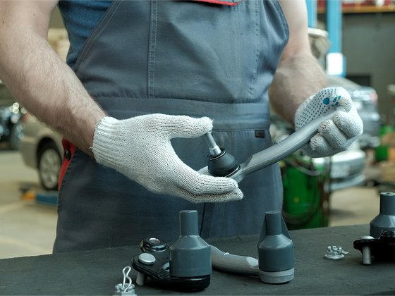 Mann an einem Tisch, der einen Spurstangenkopf in der Hand hält und prüft. Auf dem Tisch liegen weitere Spurstangenköpfe