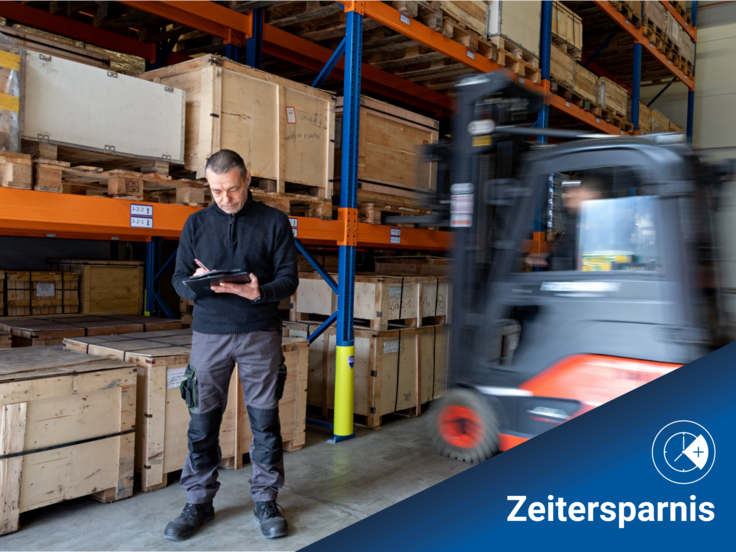 Zwei Kollegen arbeiten im Lager. Der eine steht vor einem Lagerregal und bearbeitet eine Materialliste. Der andere fährt Gabelstapler und lagert Ware ein.