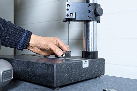 Hand measures small metal part with height gauge on measuring table