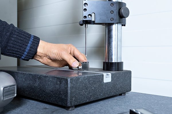 Hand misst kleines Metallteil mit Höhenmessgerät auf Messtisch
