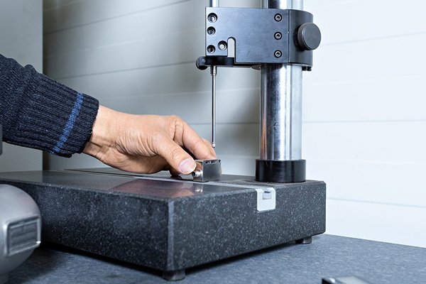 Hand measures small metal part with height gauge on measuring table