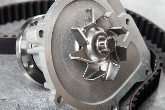 Wasserpumpe für Autos mit Dichtung und Zahnriemen auf grauem Tisch.