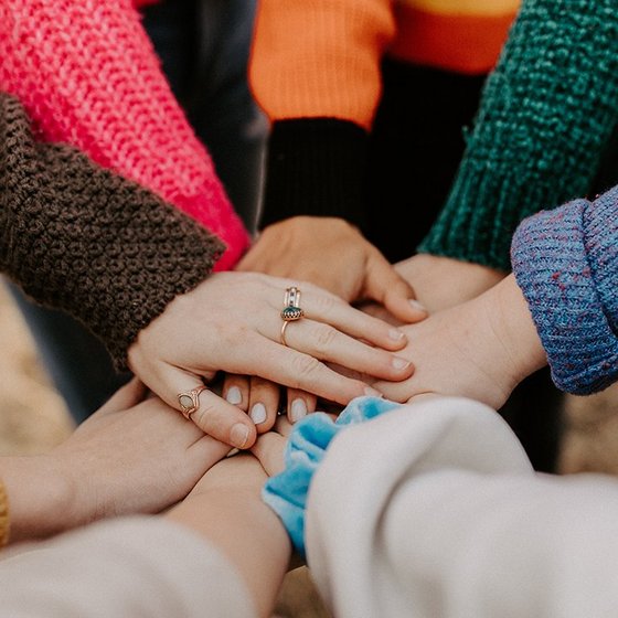 Unterschiedliche Hände, die sich in der Mitte treffen, aufeinanderliegen und Zusammenhalt symbolisieren.